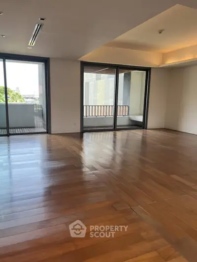 Spacious living room with wooden flooring and large windows leading to a balcony.