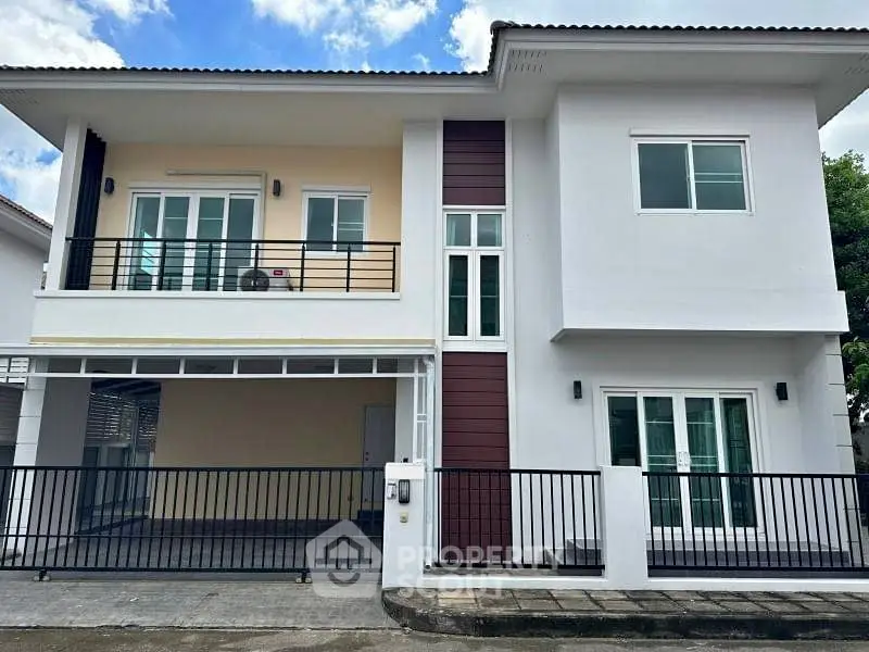Modern two-story house with balcony and gated driveway, ideal for family living.