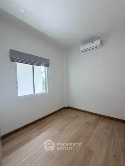 Minimalist empty room with wooden flooring and air conditioning unit, perfect for customization.