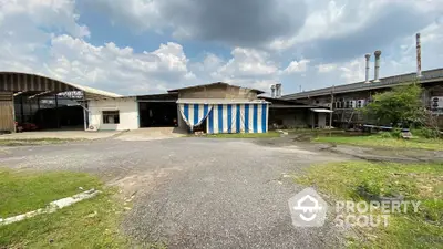 Industrial warehouse exterior with spacious parking area under a cloudy sky.