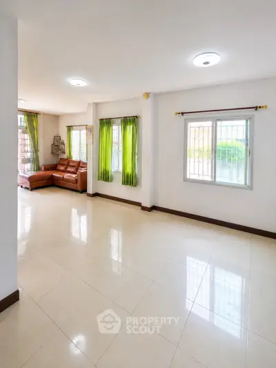 Spacious living room with tiled floors and natural light, featuring a cozy leather sofa and vibrant green curtains.