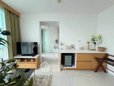 Modern living room with sleek furniture and natural light, featuring a TV and mini fridge.