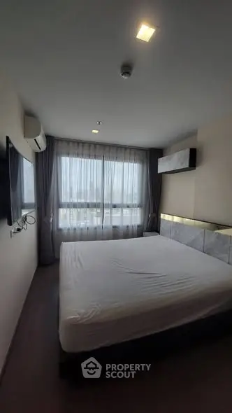 Spacious bedroom with large window and modern decor in a high-rise apartment.