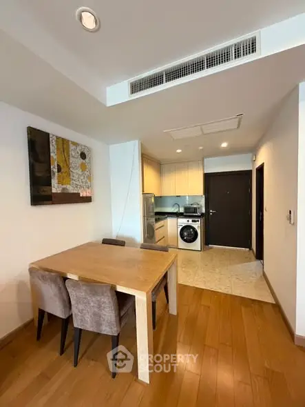 Modern dining area with wooden flooring and compact kitchen featuring washing machine.
