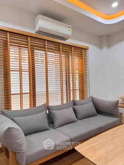 Modern living room with stylish gray sofa and wooden blinds, featuring a sleek air conditioning unit.