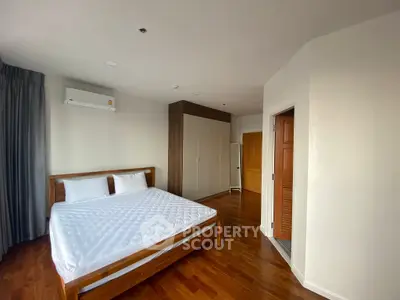 Spacious bedroom with wooden flooring and modern furnishings in a bright apartment.