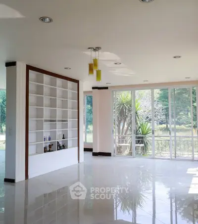 Spacious living room with large windows and built-in shelving, offering abundant natural light and garden views.