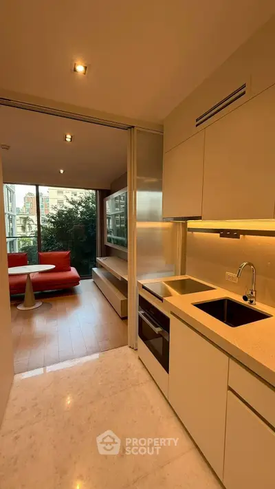 Modern open-layout kitchen with sleek cabinetry and cozy living area, featuring large windows and stylish furnishings.