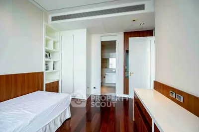 Modern bedroom with sleek wooden flooring and built-in storage, leading to a stylish bathroom.