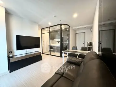 Modern living room with sleek black furniture and glass partitioned kitchen