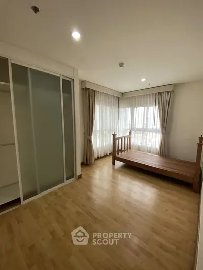 Spacious bedroom with wooden flooring and large windows for natural light.