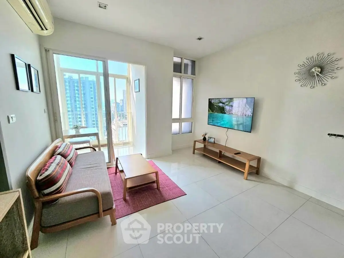 Modern living room with balcony view in a high-rise apartment, featuring sleek furniture and a wall-mounted TV.