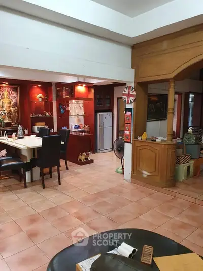 Spacious living area with dining set and fridge, featuring warm lighting and tiled flooring.