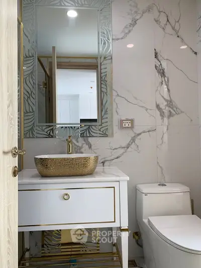 Luxurious bathroom with elegant marble walls and gold accents, featuring a stylish vanity and modern fixtures.