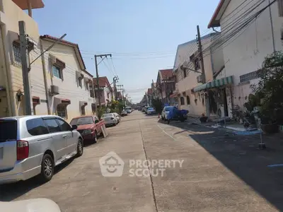 Charming residential street with parked cars and row houses under clear blue sky.