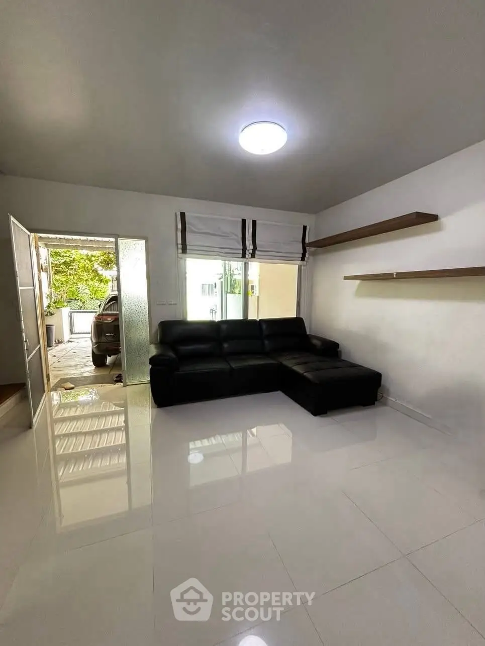 Spacious living room with modern black sofa and natural light, perfect for relaxation.