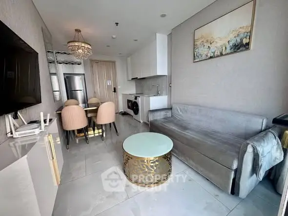 Modern living room with elegant decor, featuring a stylish chandelier, sleek furniture, and integrated kitchen appliances.