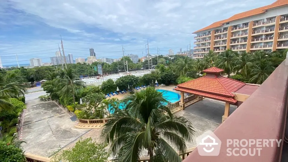 Stunning resort-style pool view from balcony with lush greenery and city skyline backdrop.