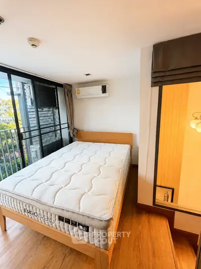 Modern bedroom with large windows and wooden flooring, featuring a comfortable bed and air conditioning.