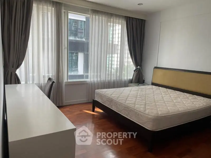 Spacious bedroom with large window and elegant furnishings in modern apartment.