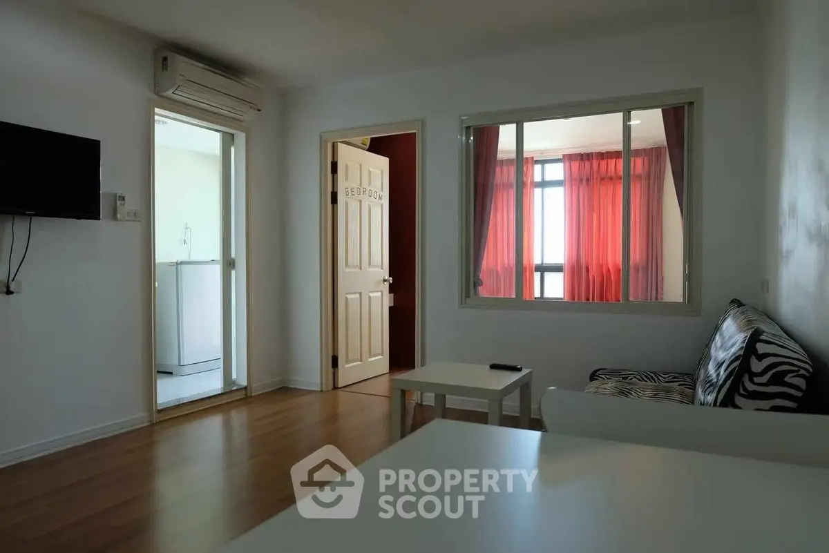Modern living room with zebra-patterned sofa and red curtains, featuring a view into the bedroom.
