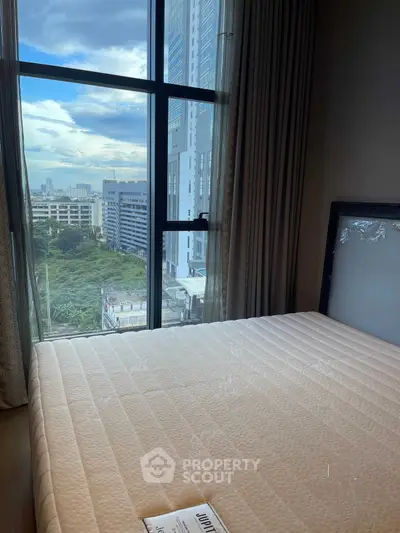 Spacious bedroom with large window offering stunning city view in modern high-rise apartment.
