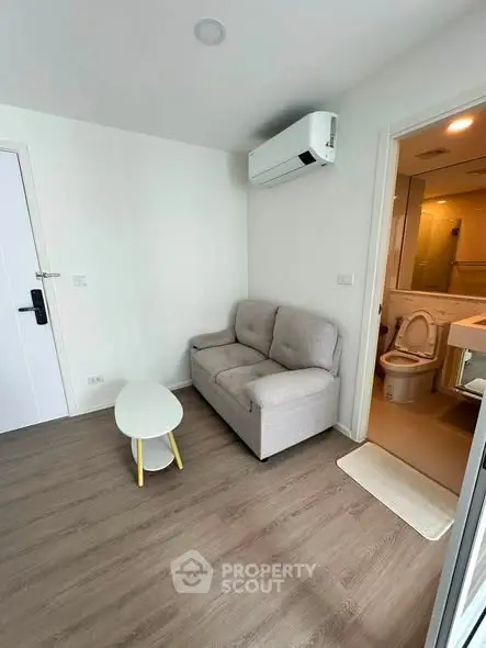 Cozy living room with modern sofa, air conditioning, and adjacent bathroom in a compact apartment.