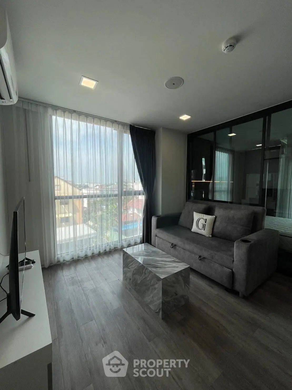 Modern living room with large window, stylish sofa, and sleek TV setup in a contemporary apartment.