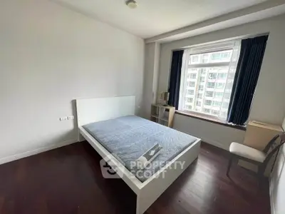 Spacious bedroom with large window and modern furnishings in a high-rise apartment.