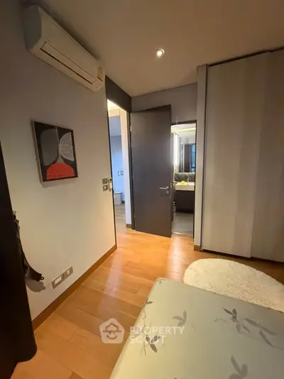 Cozy bedroom with wooden flooring and modern decor, featuring a stylish air conditioning unit and a glimpse into the bathroom.