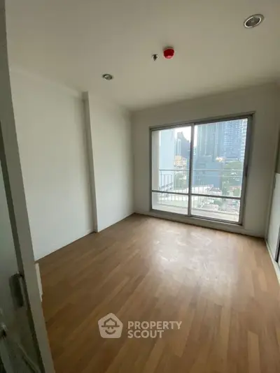 Bright empty room with wooden flooring and city view from large window.