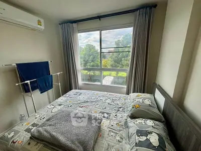 Cozy bedroom with large window offering lush green views, featuring modern decor and air conditioning.