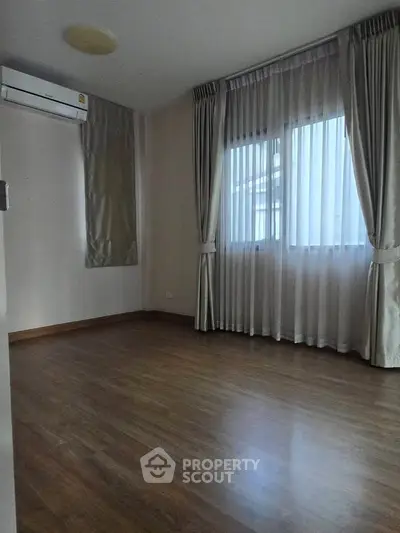 Spacious empty room with wooden flooring and large windows, perfect for customization.