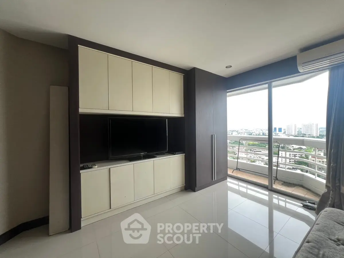 Spacious living room with modern entertainment center and city view balcony.