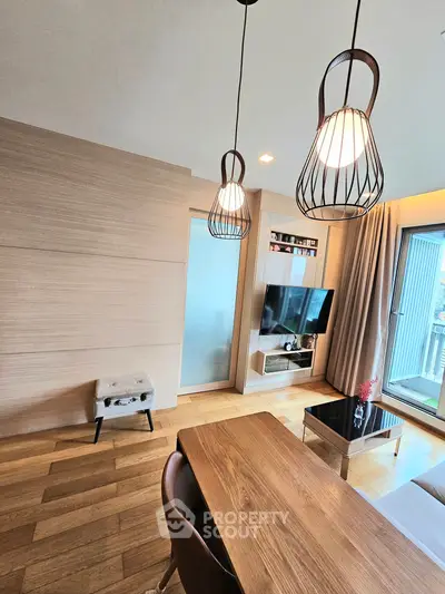 Modern living room with stylish lighting and wooden flooring, featuring a cozy TV area and balcony access.