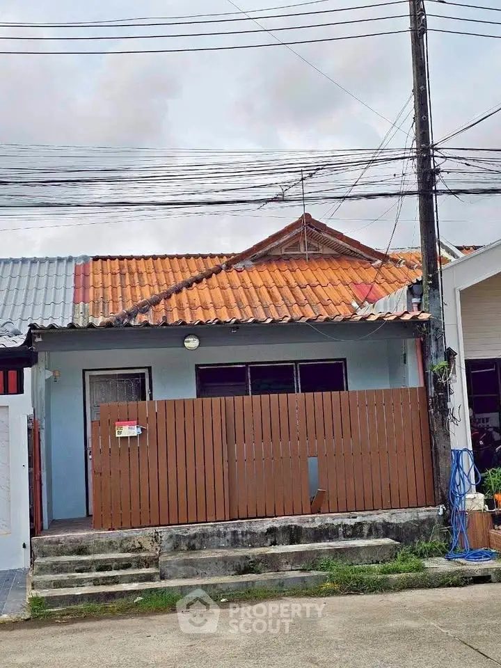 Charming single-story house with tiled roof and fenced front yard in a quiet neighborhood.