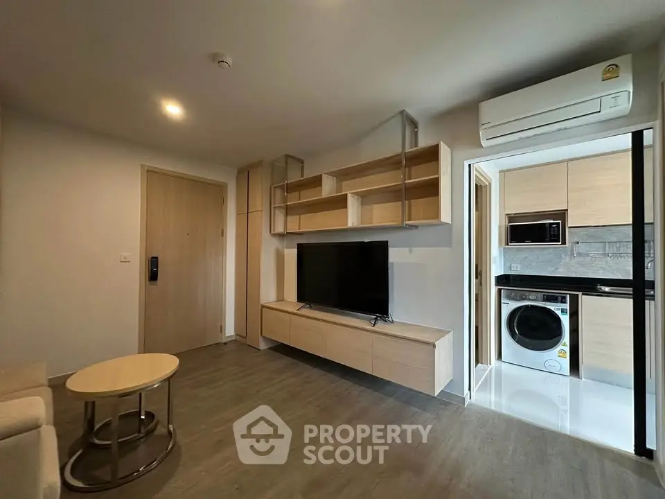 Modern living room with TV, open kitchen, and washing machine in stylish apartment.