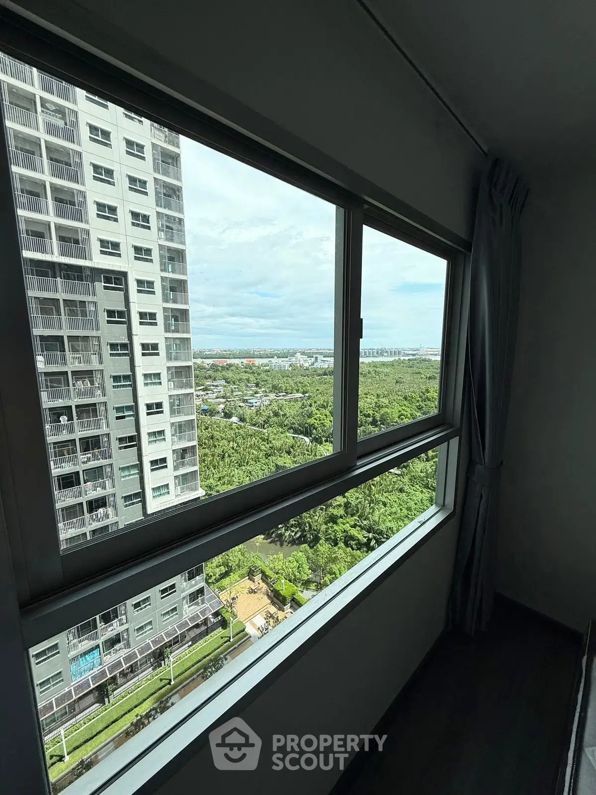 High-rise apartment window view with lush greenery and cityscape in the distance.