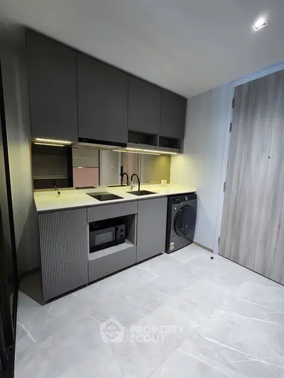 Modern kitchen with sleek cabinetry and built-in appliances, featuring a washing machine and stylish lighting.