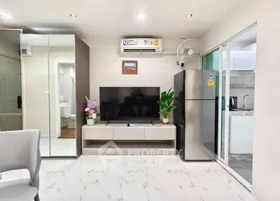 Modern living room with sleek TV setup and stainless steel fridge in open layout apartment.