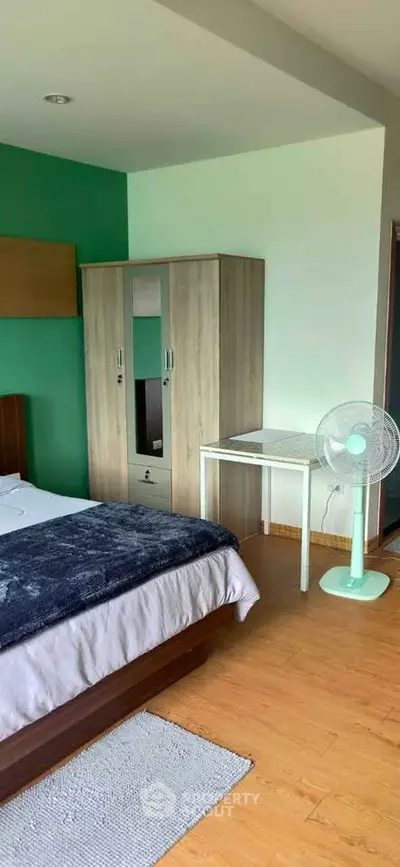 Cozy bedroom with wooden flooring, modern wardrobe, and a fan for comfort.