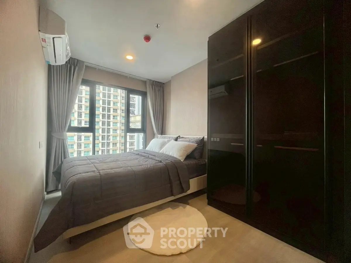Modern bedroom with large window and city view, featuring sleek wardrobe and cozy bedding.