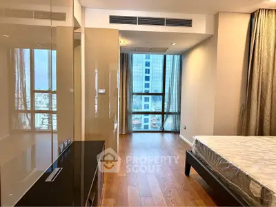 Spacious modern bedroom with large window and city view, featuring elegant wooden flooring and neutral decor.
