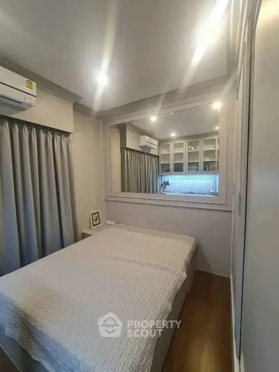 Cozy bedroom with modern decor and large mirror enhancing space.