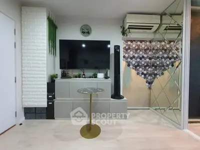 Modern living room with stylish decor and large TV, featuring mirrored wall and air conditioning units.