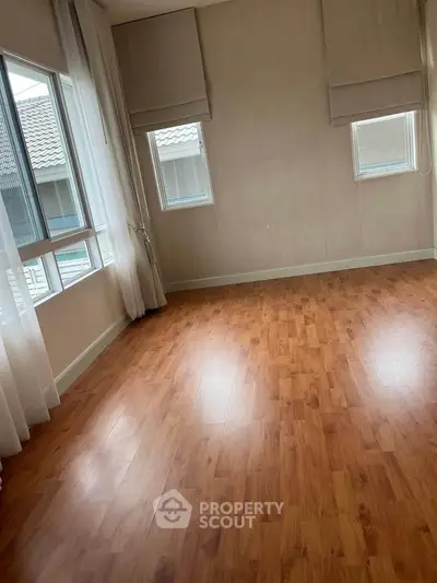 Spacious empty room with wooden flooring and large windows for natural light.