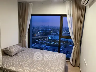 Cozy bedroom with large window offering stunning cityscape view at dusk.