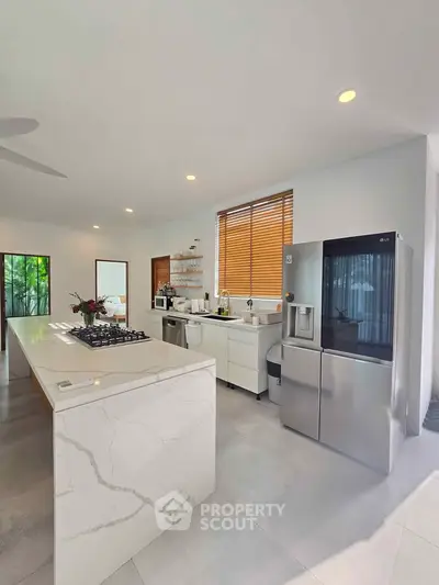 Modern kitchen with marble island and stainless steel appliances in bright open layout.