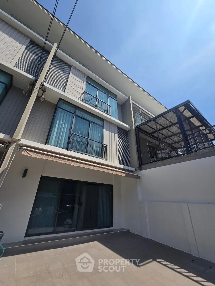 Modern three-story townhouse with large windows and balcony under clear blue sky