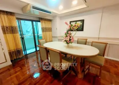 Elegant dining room with polished wooden floors and floral centerpiece, featuring a sliding glass door to a balcony.